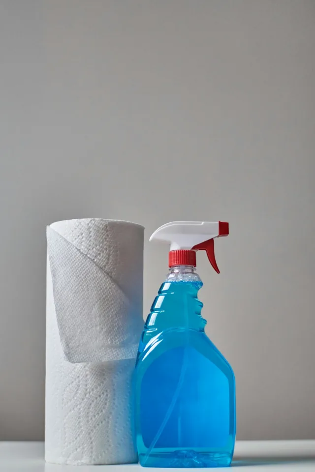 Clear spray bottle with blue liquid beside a roll of paper towels